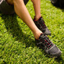 Person sitting on grass wearing grey and red trail trainers with cushioned soles for outdoor comfort.