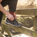 Person tying laces of grey and red waterproof walking shoes on a wooden bridge in natural sunlight.