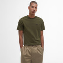 A man in olive green T-shirt and beige trousers stands with hands in pockets against a white background, conveying a relaxed and casual vibe.