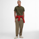 Young man in an olive green T-shirt and beige pants, with a red jumper tied at the waist. Neutral expression, set against a plain white background.