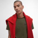 Young man wearing a green Barbour t-shirt with a red jumper draped over his shoulders. He stands against a neutral background, looking confident.