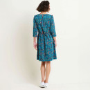 Woman in a blue patterned dress facing away on a white background.