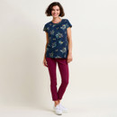 Woman in blue floral top and maroon pants standing against a neutral background.