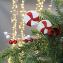 Festive ornaments with red glitter swirls and white accents are nestled on a green pine branch, set against a backdrop of soft, warm fairy lights.
