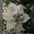 Sparkling silver ornament with berries and a white poinsettia adorn a Christmas tree. Warm fairy lights create a festive, elegant atmosphere.