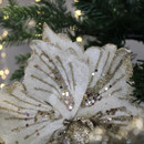 Sparkling white flower ornament with gold glitter and sequins, nestled in a green tree, surrounded by warm, blurred lights; festive and elegant.