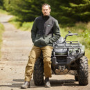 A person standing beside an ATV on a dirt trail surrounded by greenery.