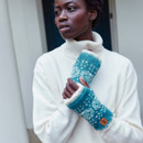 Woman in a white turtleneck jumper looks to the side, wearing turquoise and white patterned fingerless gloves. The expression is serene and thoughtful.