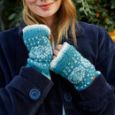 A woman smiles warmly, wearing a navy coat and teal knit mittens with white patterns and fuzzy lining. The soft, cosy textures convey warmth and comfort.