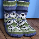 Knitted wool socks with green, blue, and white stripes feature a repeated sheep pattern. Socks are worn over pants, exuding a cosy, whimsical vibe. Knitted wool socks with green, blue, and white stripes feature a repeated sheep pattern. Socks are worn over pants, exuding a cosy, whimsical vibe.