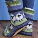 Cosy knitted slipper socks with a sheep pattern, featuring green and white colours and fluffy white cuffs, rest on a wooden floor, conveying warmth and comfort. Cosy knitted slipper socks with a sheep pattern, featuring green and white colours and fluffy white cuffs, rest on a wooden floor, conveying warmth and comfort.
