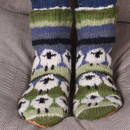 Cosy wool socks with sheep patterns in blue, green, white, and black tones. The socks exude warmth and comfort against a grey, textured background. Cosy wool socks with sheep patterns in blue, green, white, and black tones. The socks exude warmth and comfort against a grey, textured background.
