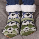 Cosy, patterned socks with white fleece cuffs feature green and purple abstract floral design, worn against a grey textured blanket for a warm feel. Cosy, patterned socks with white fleece cuffs feature green and purple abstract floral design, worn against a grey textured blanket for a warm feel.