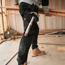 Side view of black work trousers in use on a construction site, showing tool pocket with hammer and reinforced panels