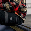 Close-up of black work trousers with Hard Yakka branding, worn with flannel shirt and reinforced knee area