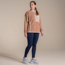 Full-body studio shot of woman wearing navy leggings with a beige fleece pullover and trainers.