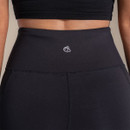 Close-up of the rear waistband on women's black high-waisted performance leggings, featuring a smooth supportive waistband and reflective logo detail.