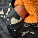 Close-up of a hand in a camo jacket pocket lined with orange fleece. The mix of dark and light camo patterns contrasts with the vibrant fleece. Cosy and warm feel.