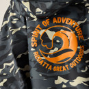 Smiling child with curly hair wearing sunglasses and a camo-patterned jacket with bright orange lining. The pose conveys joy and confidence.