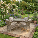 Wicker dining set on a stone patio surrounded by lush, colorful garden blooms and greenery, creating a serene and inviting outdoor atmosphere.
