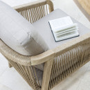 A close-up view of a rope-weave lounge chair with soft grey cushions and an open book resting on the seat.
