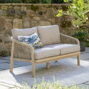 A rope-weave two-seater outdoor sofa with light grey cushions placed on a patio beside a rustic stone wall.