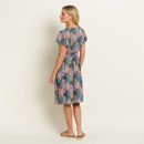Woman in floral dress standing sideways on a neutral background.