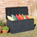 Black slatted garden storage box with the lid open, filled with colourful outdoor cushions against a brick wall.