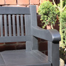 Close-up of the armrest and slatted backrest of a black plastic garden storage bench beside potted plants.