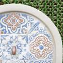Close-up of a ceramic plate featuring intricate blue and brown geometric patterns. The background is a lush, green textured surface.