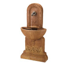 A rustic stone wall fountain with arched top, water gently flowing from a spout into a basin below. The design evokes a calm, classical feel.