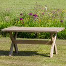 Rectangular wooden garden table with sturdy curved legs, placed on a lawn with a flower bed behind.
