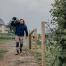Worker carrying wire fencing wearing beige Hard Yakka trousers with reinforced knees and multiple pockets on rural worksite