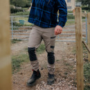 Hard Yakka beige work trousers worn outdoors, featuring black reinforced knee panels, cargo pockets and durable stretch fabric