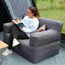 A person reading a book while sitting on a cosy gray couch in a tent, surrounded by greenery.