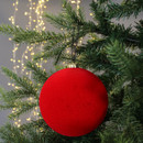 A vibrant red Christmas ornament hangs on a lush green tree with twinkling lights in the background, creating a festive and joyful atmosphere.