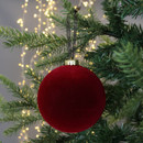 A large red ornament hangs on a Christmas tree branch, surrounded by glowing fairy lights. The scene conveys a festive and warm holiday atmosphere.