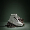 Light grey winter hiking boot displayed on rugged natural debris against a dark green background, highlighting its outdoor design.