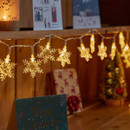 String lights shaped like snowflakes illuminate a cozy wooden shelf adorned with holiday cards and decorations.