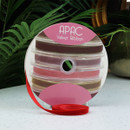 A spool of red velvet ribbon on a grey surface with a plant background.
