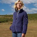 A woman in a blue fleece jacket stands in an open grassy field under a clear blue sky. She appears confident and relaxed, with a gentle breeze blowing.