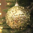 Rosemary Green Sequin & Bead Foam Bauble on a grey background with a christmas tree and lights