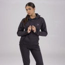 Woman in a charcoal coloured hoodie and matching joggers standing against a white background holding both hood drawstrings in her hands.