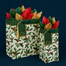 Two holly print Christmas gift bags in different sizes with dark green ribbon handles, gold-edged gift tags and red, green and gold tissue paper.
