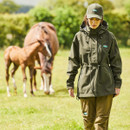 A woman wearing a green smock with a horse and pony in the background