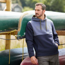 Man leaning against a rack of upturned canoes wearing a Ridgeline Men's South Island Hoodie in a two-tone Navy colour