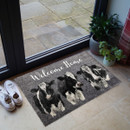 Welcome mat near glass doors with three cows and "Welcome Home" text. Sneakers and plants nearby, creating a cosy, inviting entrance.