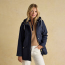 A woman wearing a navy waterproof jacket layered over a camel knit, showing gold zip detailing and flap pockets.