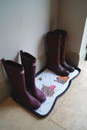 Two pairs of boots sit neatly on a white, decorative rubber mat with animal prints. The scene conveys a cosy, organized entryway.