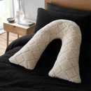 Beige diamond-textured body cushion in a v-shape on a black bedspread with a wooden bedside table and vase.